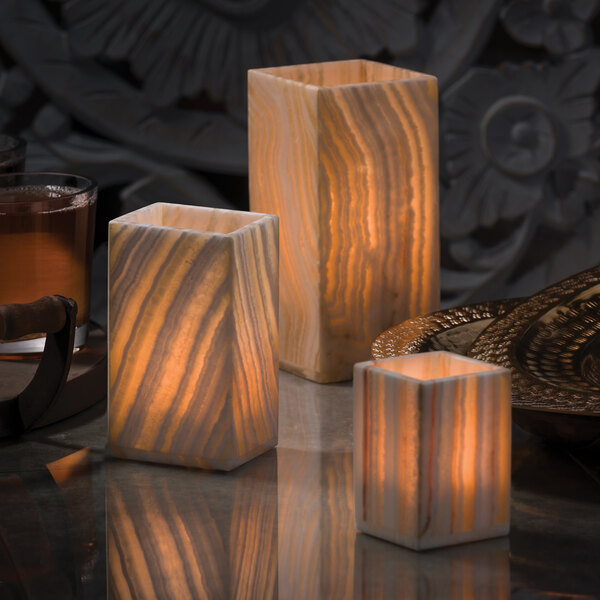 Three white marble Hollowick Luxor Alabaster candle holders on a table with lit candles.