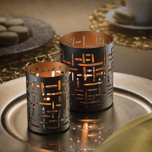 Two black and gold Hollowick cut metal votive candle holders on a plate.