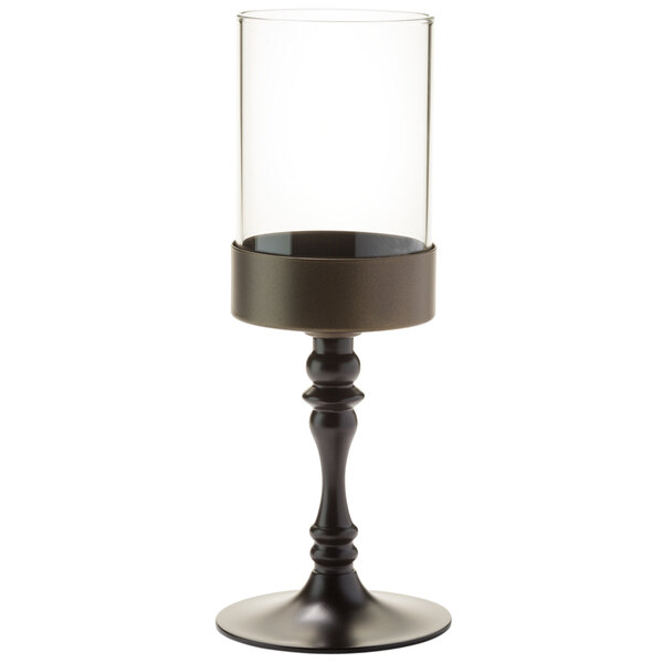 A Hollowick dark bronze candlestick with a clear glass cylinder on a stand.