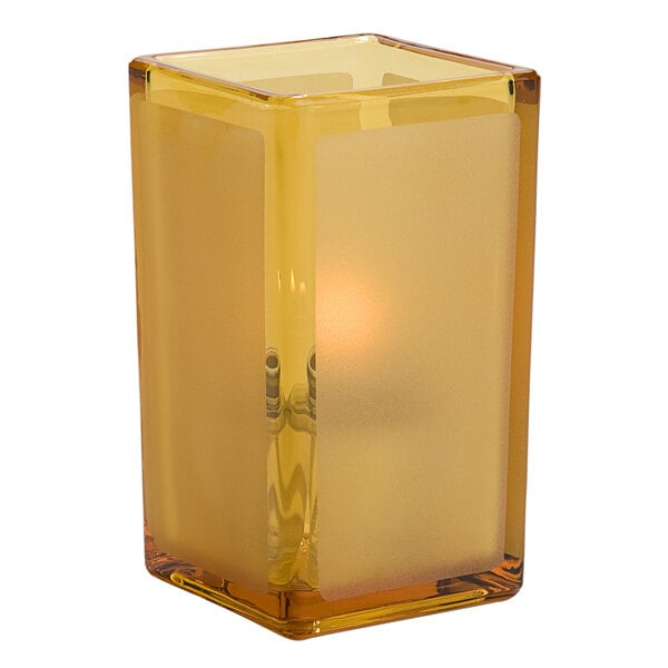 A Hollowick amber square glass candle holder with a lit yellow candle inside.