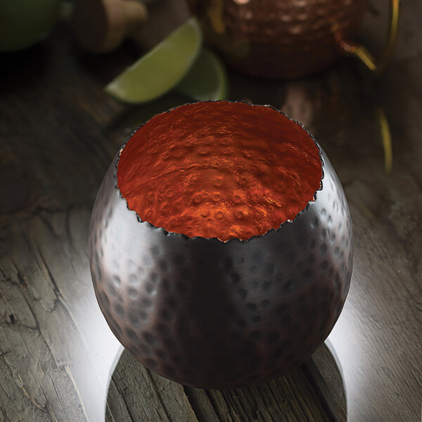 A dark bronze metal Hollowick cauldron with a copper leaf design on the outside and a red inside.