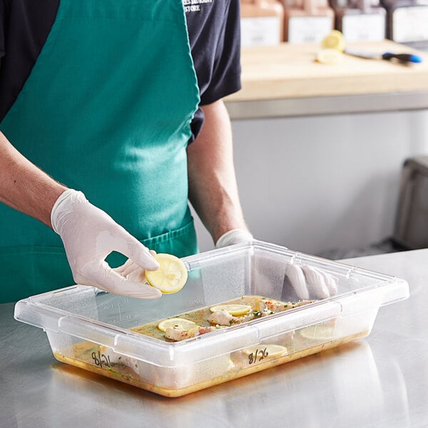A person in a green apron and gloves placing lemon slices in a Vigor clear polycarbonate food storage container.