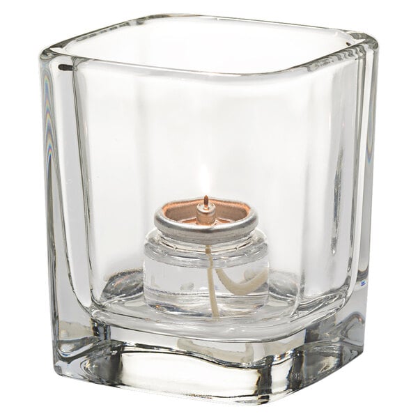 A Hollowick Tetra clear glass square votive with a candle inside.