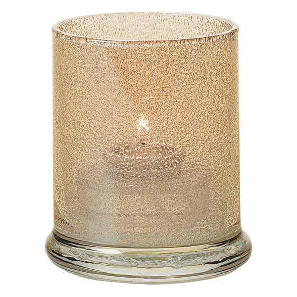 A Hollowick champagne jewel glass votive column with a lit candle inside.