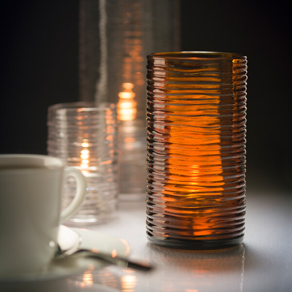 A dark amber glass cylinder candle holder with a lit candle inside.