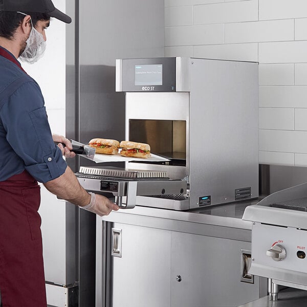 A man in a blue apron using a knife to cut a sandwich in a TurboChef Eco ST rapid cook oven.