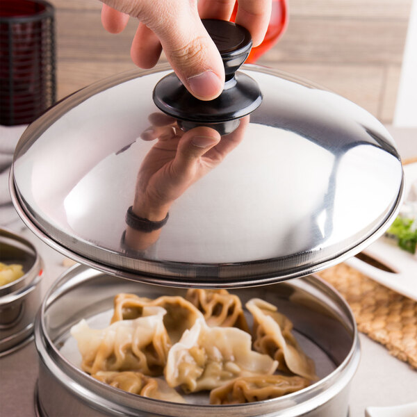 A hand holding a Town stainless steel dim sum steamer cover over a pot of dumplings.