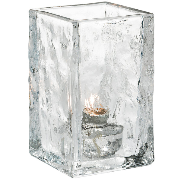 A Hollowick Glacier clear glass votive with a lit candle inside.
