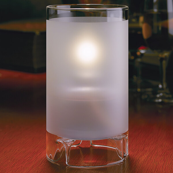 A large clear glass cylinder candle holder with a lit candle inside.