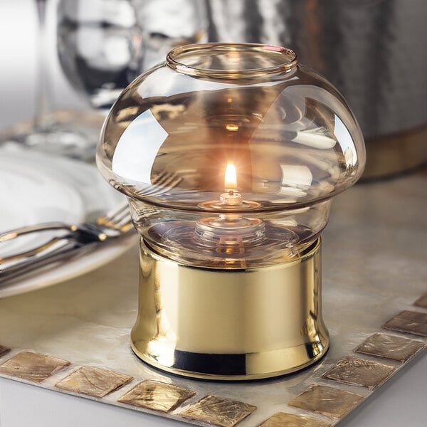 A Hollowick Amber Luster glass candle holder with a lit candle on a table.