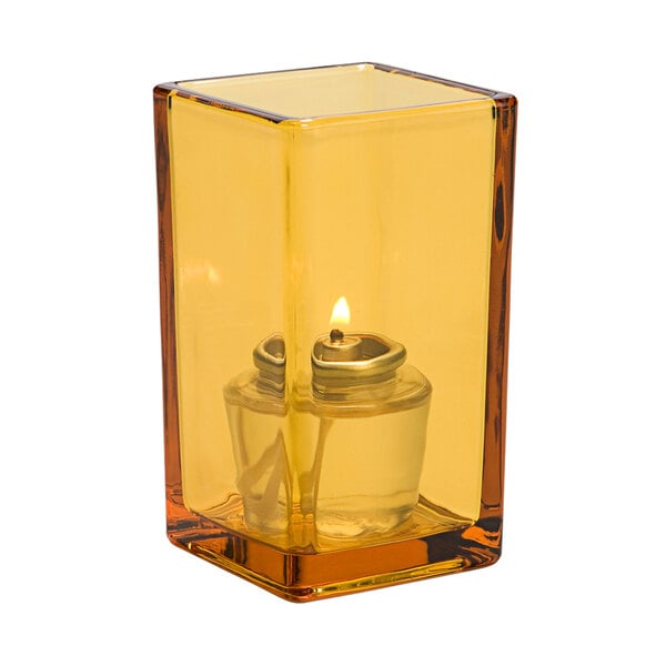 A yellow candle in a square amber glass container.
