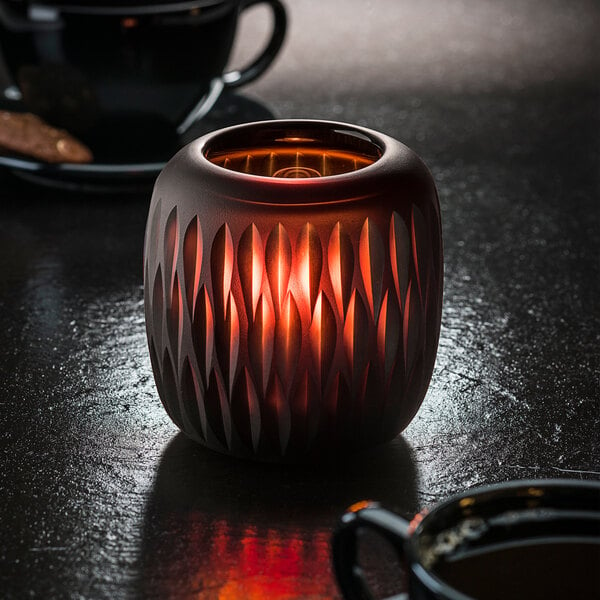 A Hollowick 4100 Mystic Black and Amber Glass Votive with a lit candle on a table in a coffee shop.