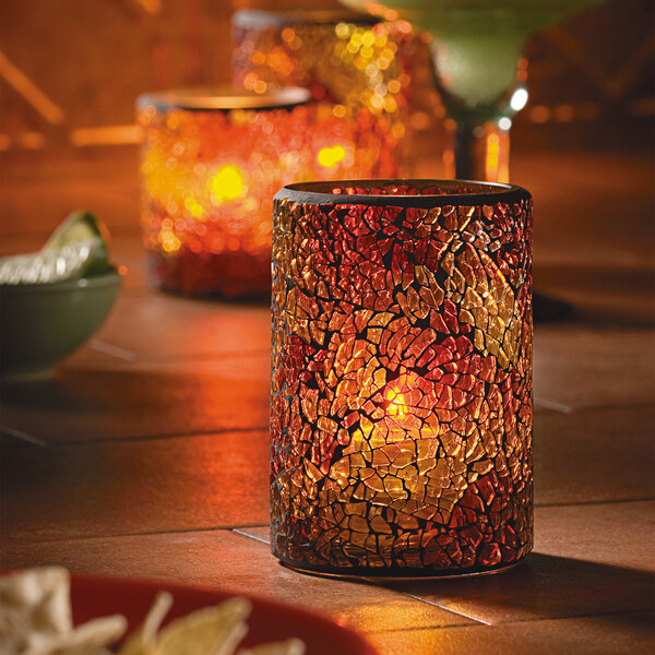 A close-up of a Hollowick crackle gold glass cylinder candle holder with a lit candle.