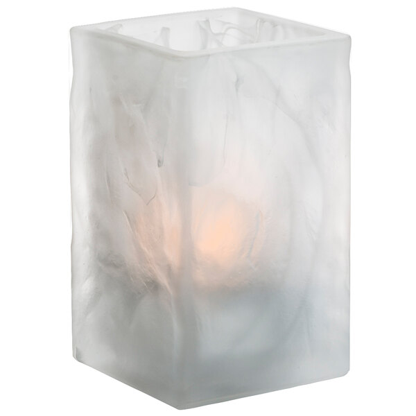 A white frosted glass Hollowick crystal votive holder with a lit candle inside.