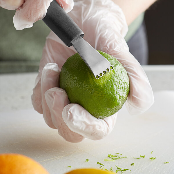 A person using a Mercer Culinary stainless steel citrus zester to peel a lime.