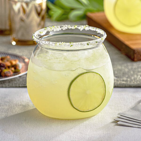 A Visions clear plastic stemless fish bowl glass with a drink and a lime slice in it on a table.