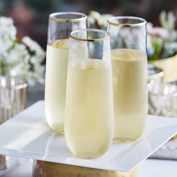 Three Visions clear plastic champagne flutes with gold trim on a white plate.