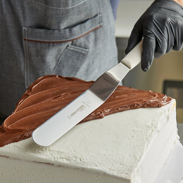 A person using a Dexter-Russell offset icing spatula to frost a cake with chocolate icing.