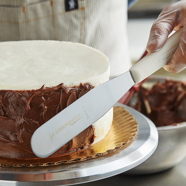 A person using a Dexter-Russell baking spatula to spread chocolate frosting on a round cake.