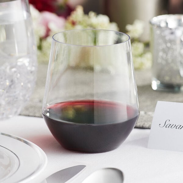 A Visions clear plastic stemless wine glass filled with red wine on a table in a catering event.
