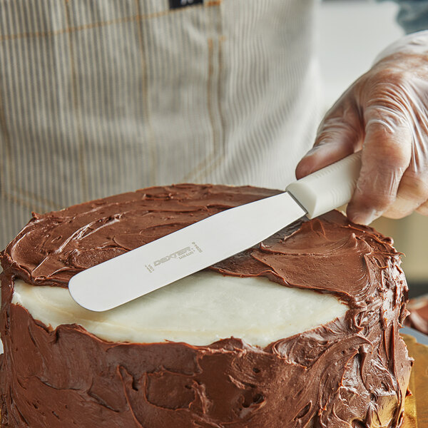 A person using a Dexter-Russell Sani-Safe baking spatula to cut a cake.