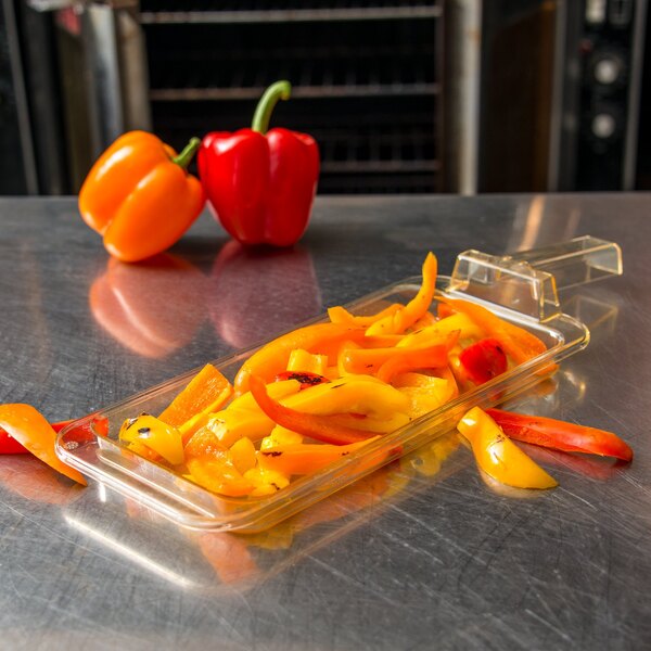A Carlisle amber plastic food pan with sliced red, yellow, and orange peppers on a table.