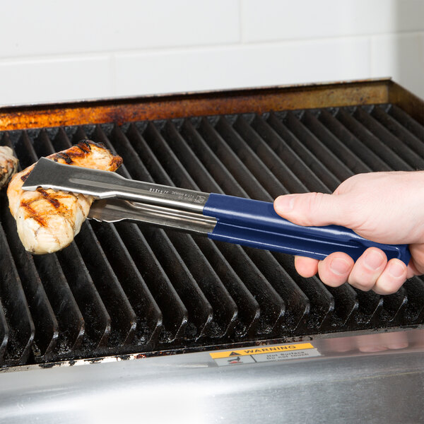 A hand holding a blue handle on a pair of Vollrath tongs over a grill.