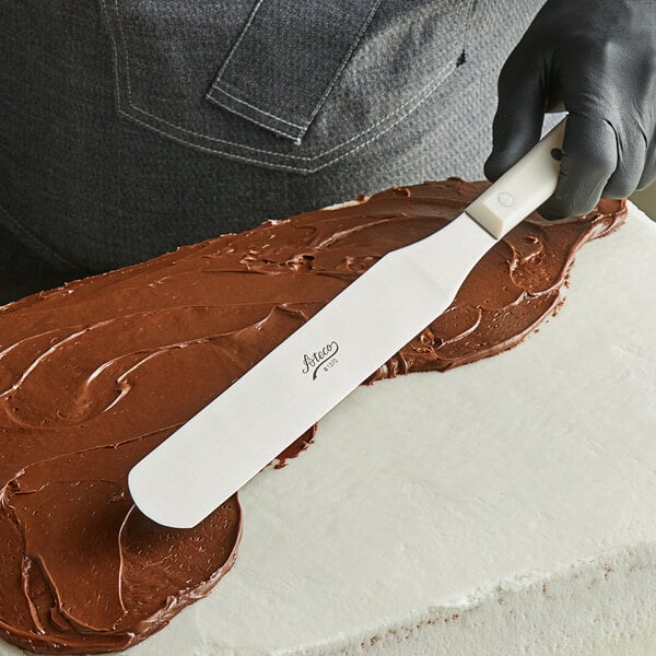 A person using an Ateco baking spatula to spread chocolate frosting on a cake.