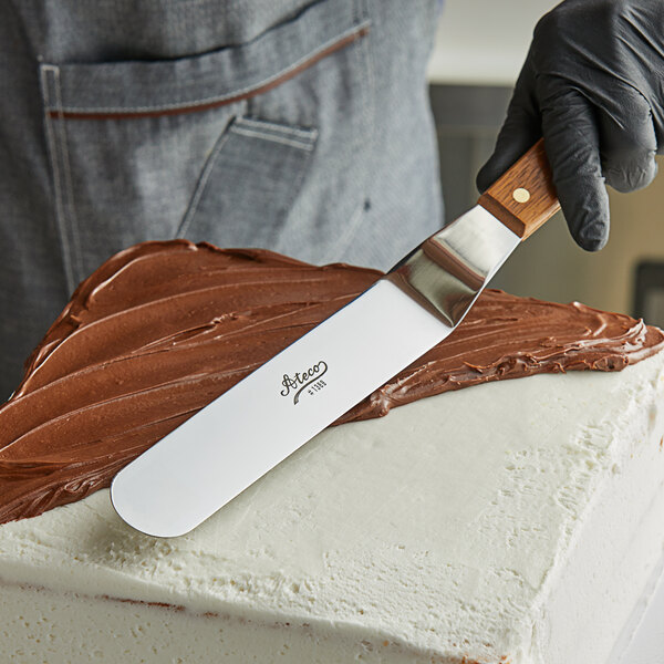 A person using an Ateco offset spatula to spread chocolate frosting on a cake.