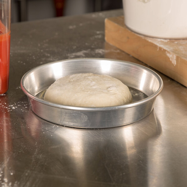 A dough ball in an American Metalcraft aluminum pizza pan on a counter.