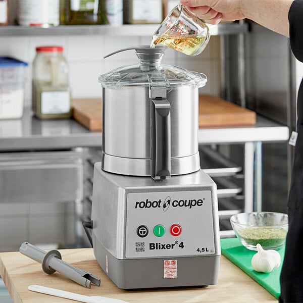A person using a Robot Coupe stainless steel food processor to make green soup.