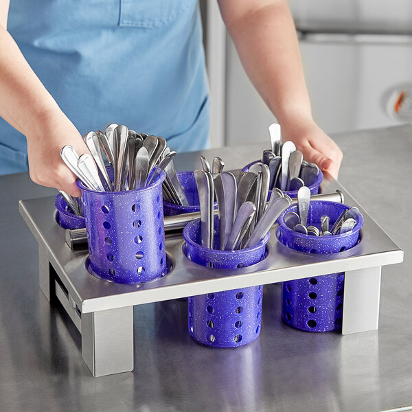A person holding a blue Steril-Sil flatware container with purple perforated cylinders full of silverware.