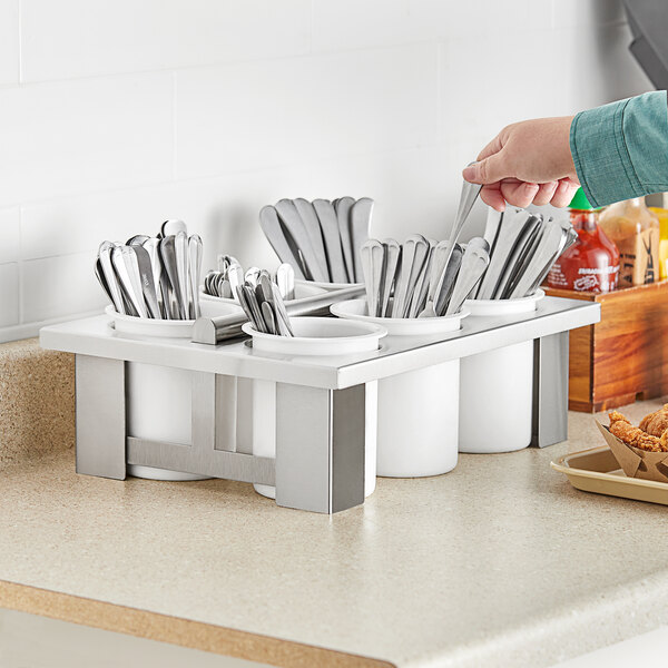 A person placing utensils in a Steril-Sil white 6-cylinder flatware holder.