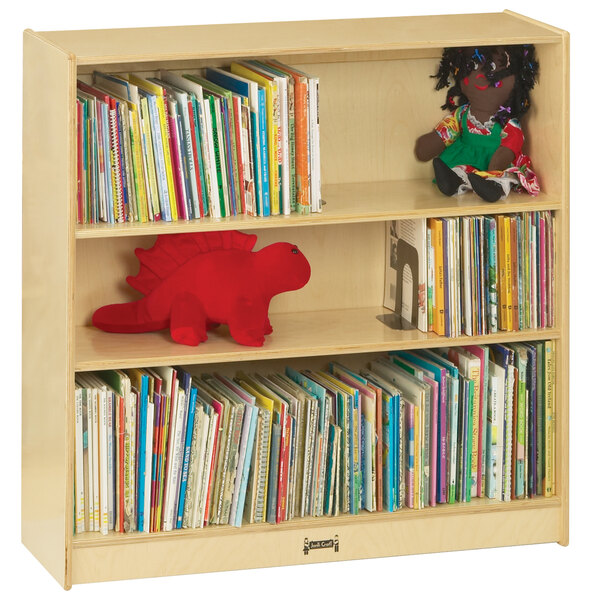 A Jonti-Craft natural wood bookcase with books and toys on the shelves.