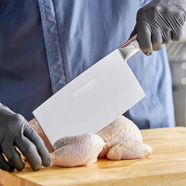 A person in gloves using a Town large stainless steel cleaver to cut raw chicken.