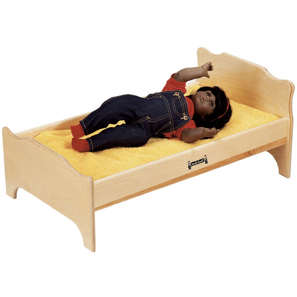 A doll lying on a Jonti-Craft wooden bed.