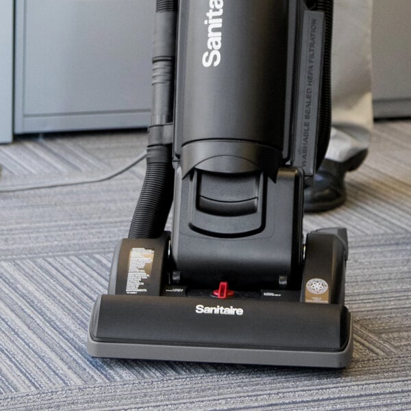 A Sanitaire bagged upright vacuum cleaner on the floor of a corporate office cafeteria.