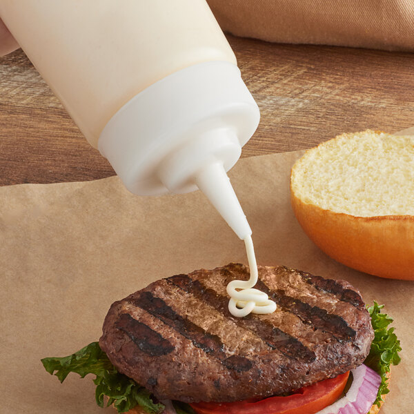 A Tablecraft clear squeeze bottle cap with a cone tip pouring sauce onto a hamburger.