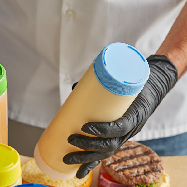 A person in black gloves using a Tablecraft light blue cap on a squeeze bottle of food.