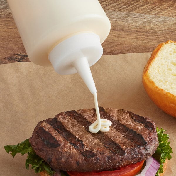A Tablecraft TipTop white cone tip cap on a squeeze bottle pouring sauce onto a hamburger.