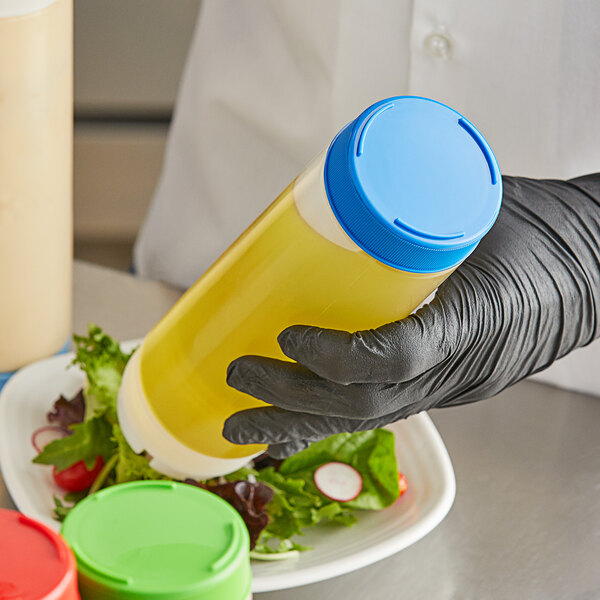 A hand in a black glove holding a Tablecraft bottle with a yellow liquid and a blue lid.