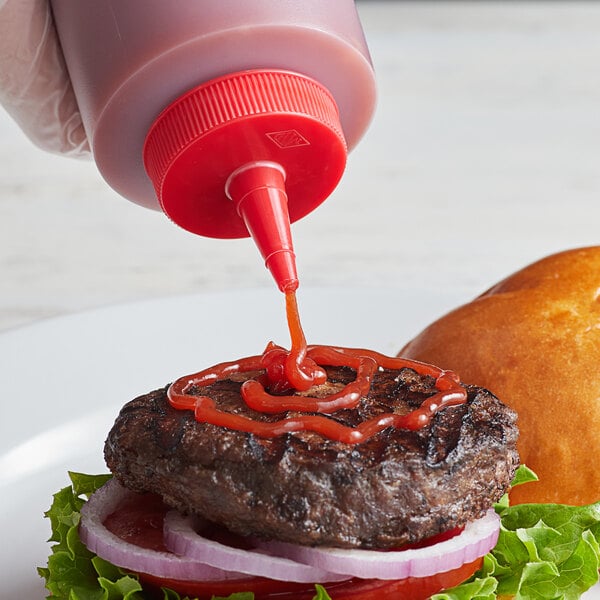A hand pouring red ketchup from a Tablecraft TipTop squeeze bottle onto a hamburger.