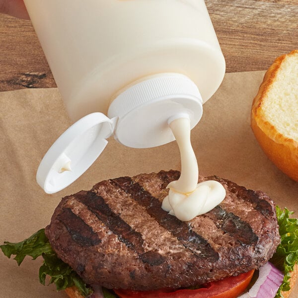 A Tablecraft white squeeze bottle cap being used to pour mayo onto a hamburger.