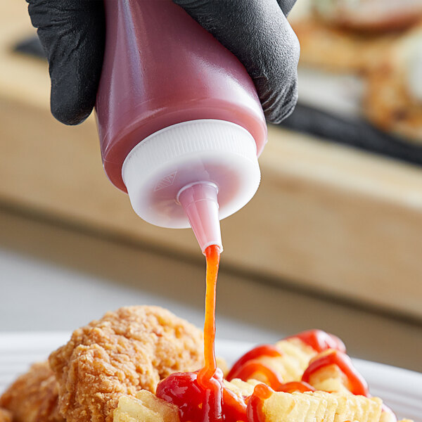 A person using a Tablecraft wide tip cap to pour ketchup onto a plate of food.