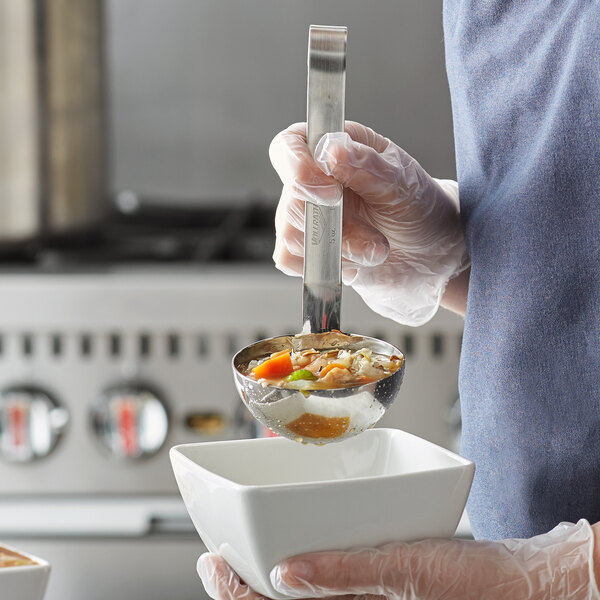 A person using a Vollrath stainless steel ladle to pour soup into a bowl.