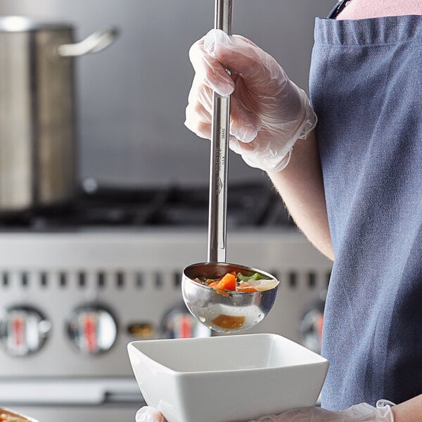 A person holding a Vollrath stainless steel ladle over a metal bowl of food.
