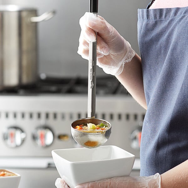 A person in a chef's uniform using a Vollrath Two-Piece Stainless Steel Ladle with a black handle to serve soup.
