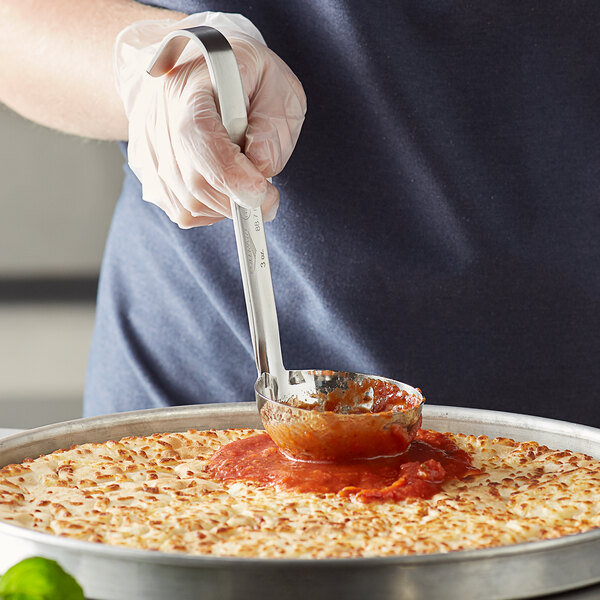 A person using a Vollrath Jacob's Pride stainless steel ladle to top a pizza with sauce.