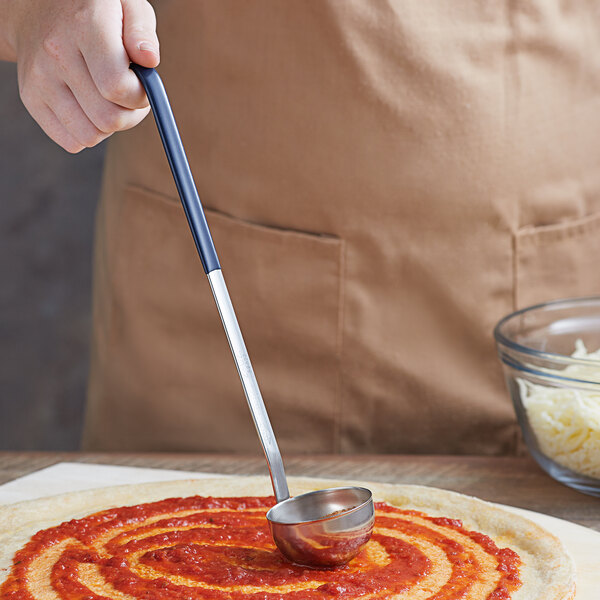 A hand holding a Vollrath stainless steel ladle with a blue Kool-Touch handle over a pizza.