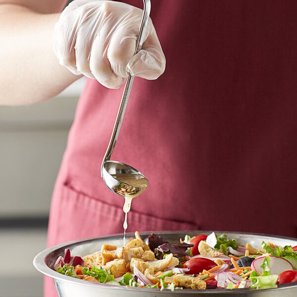 A person using a Vollrath stainless steel ladle to pour salad dressing over a bowl of salad.